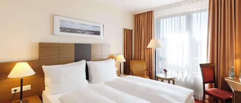 A hotel room with a large bed, two bedside tables, a desk, a chair, and a window with curtains.