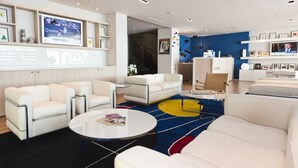 Un hall d’hôtel moderne avec des canapés en cuir blanc, une table basse ronde et un tapis aux couleurs vives.