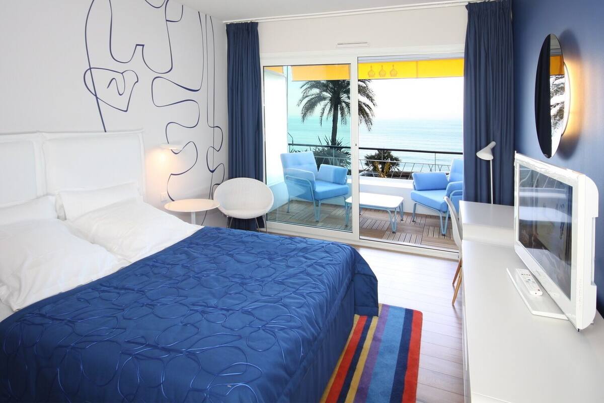 Une chambre d’hôtel comprenant un lit, un bureau avec une télévision, un balcon avec vue sur l’océan et une chaise.