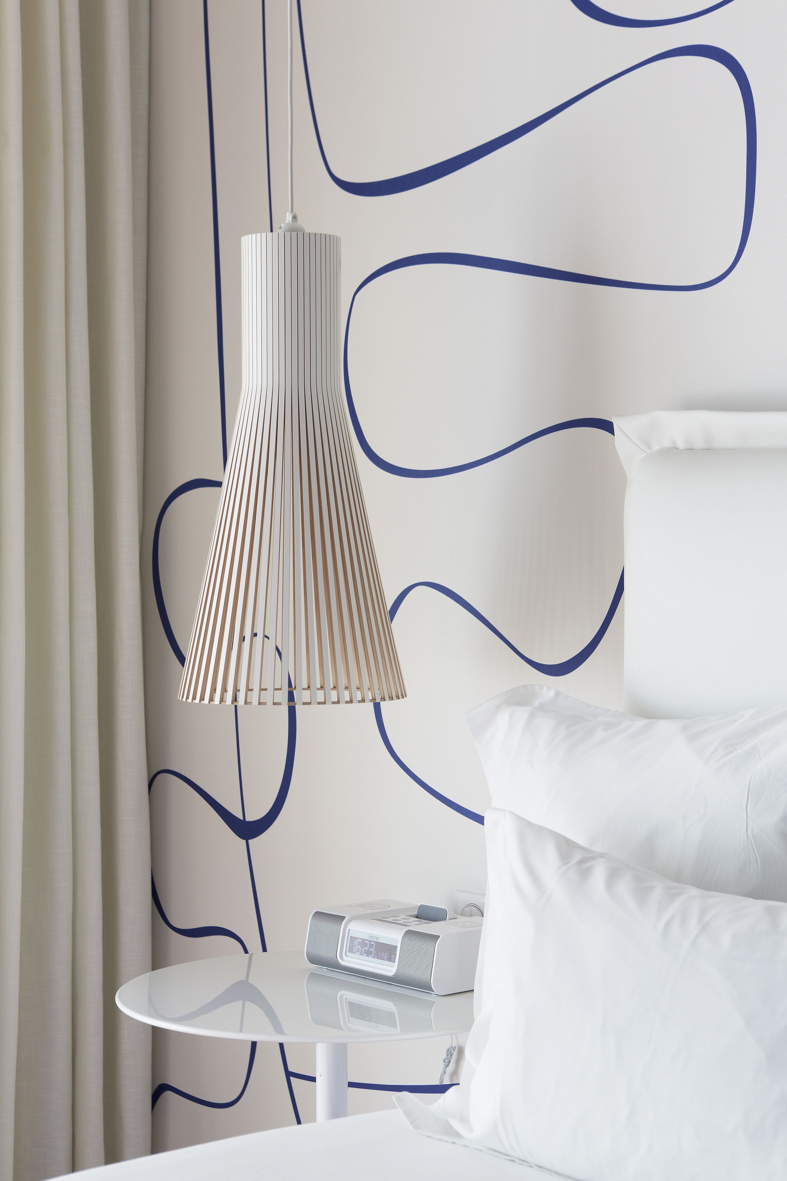 A modern bedroom with a white bed, white nightstand, and a white table with a radio.