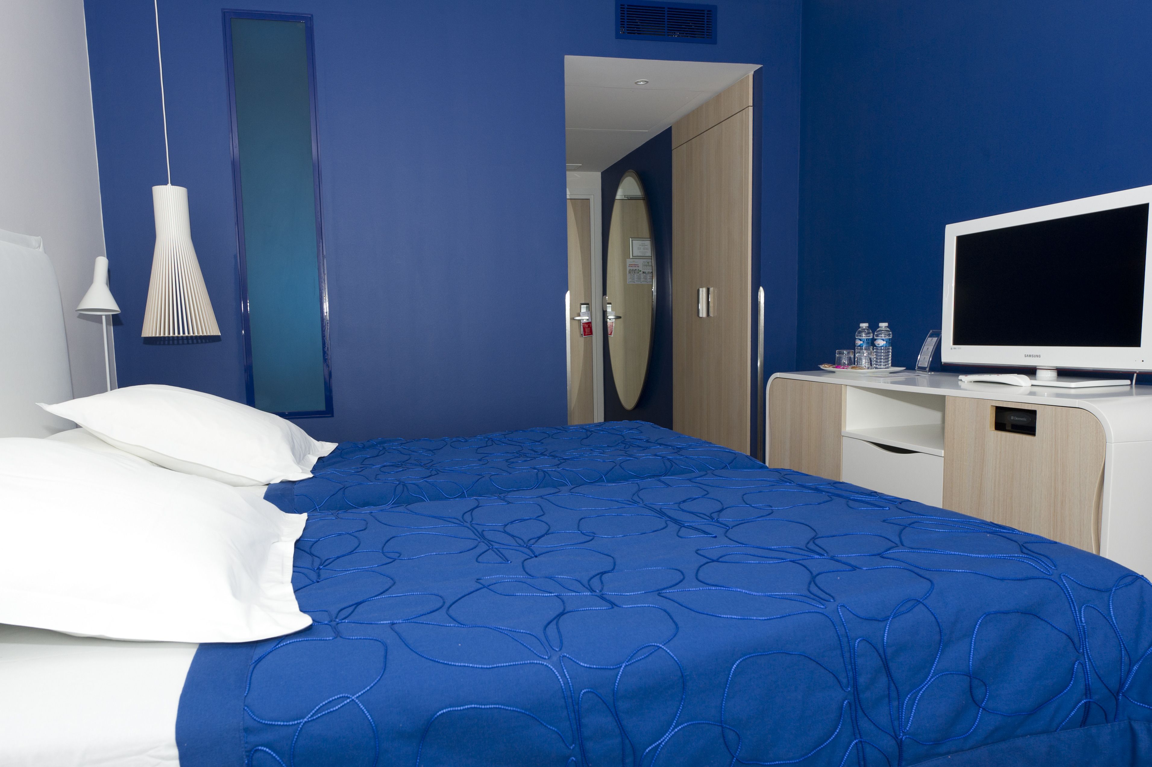 A hotel room with a large bed, a TV, a desk, and a mirror.