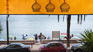 Vista de la playa con un banderín amarillo con diseños decorativos, palmeras y coches estacionados a lo largo de la orilla.