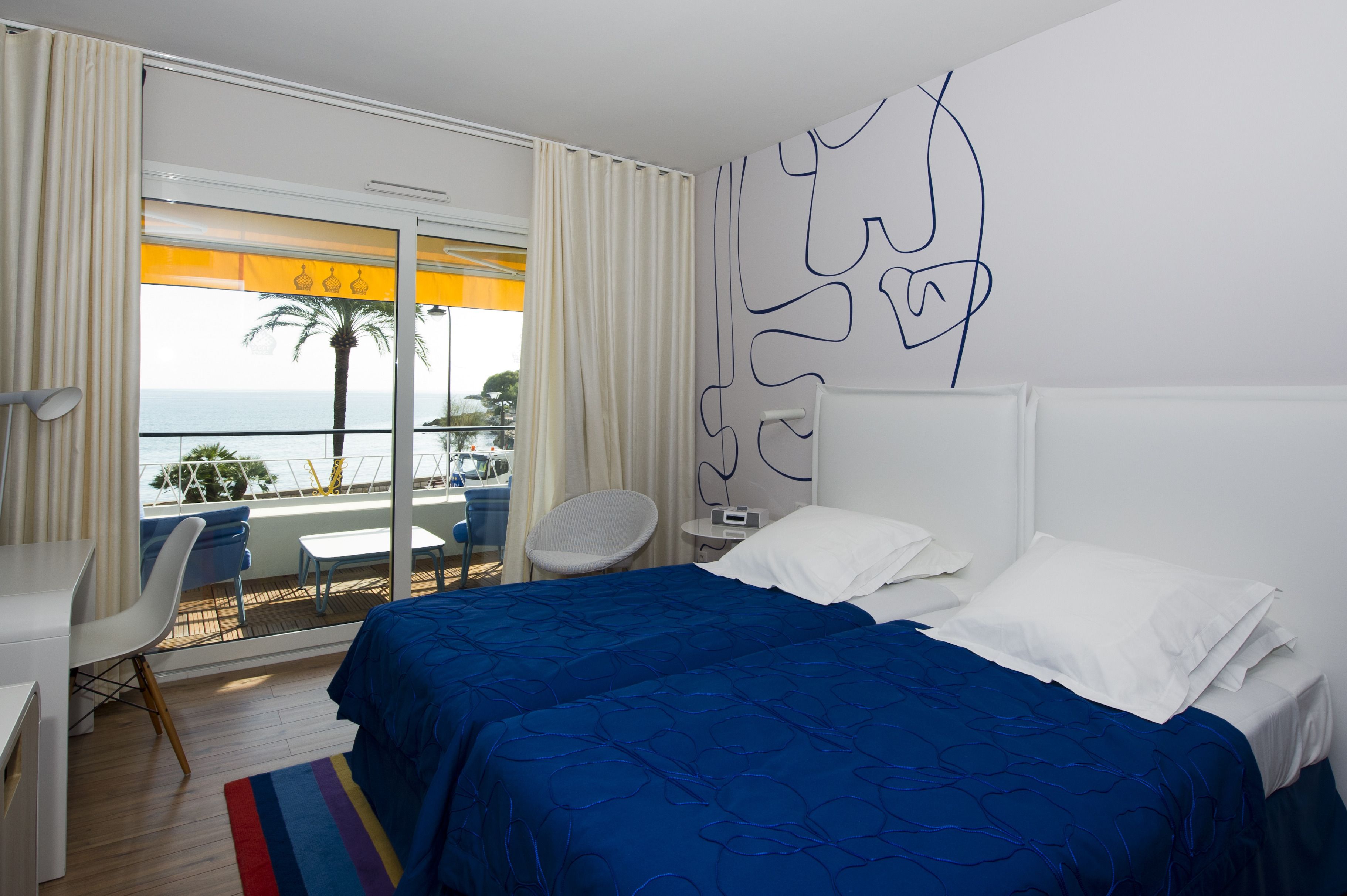 A hotel room with a bed, a desk, a chair, and a view of the ocean.