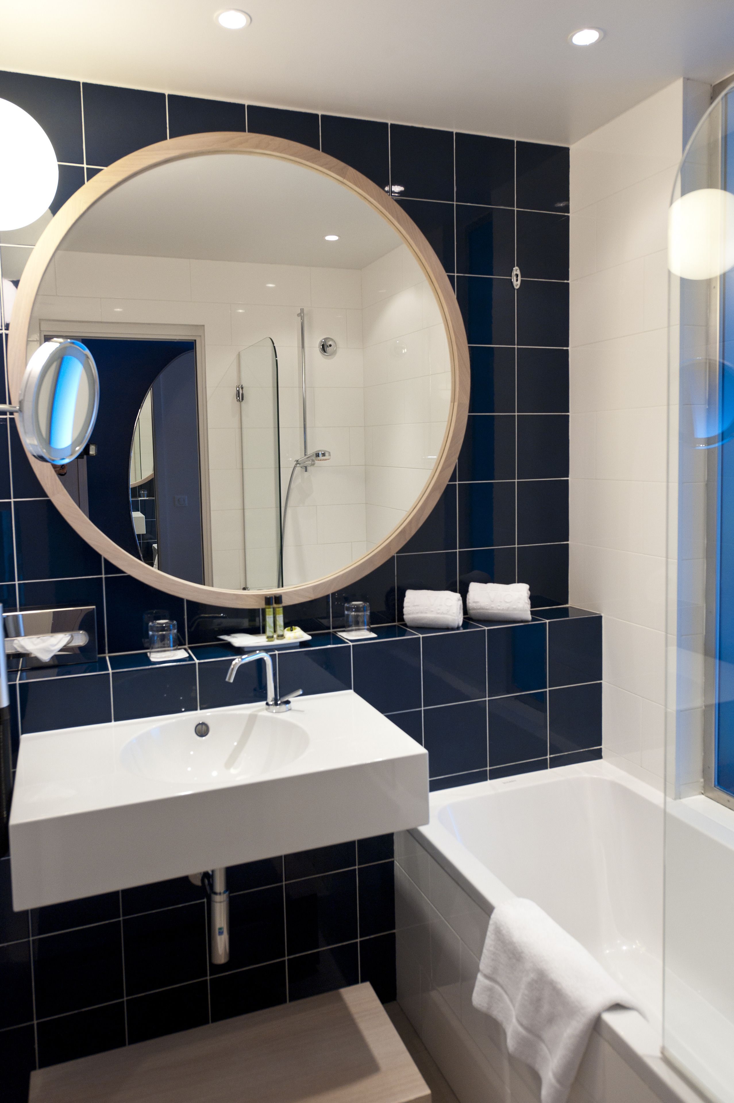 Un bagno moderno con uno specchio rotondo, un lavandino bianco e una vasca da bagno.