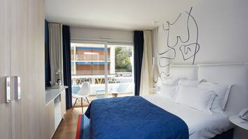 A modern hotel room with a large bed, a desk, and a balcony with a view of the building and trees.
