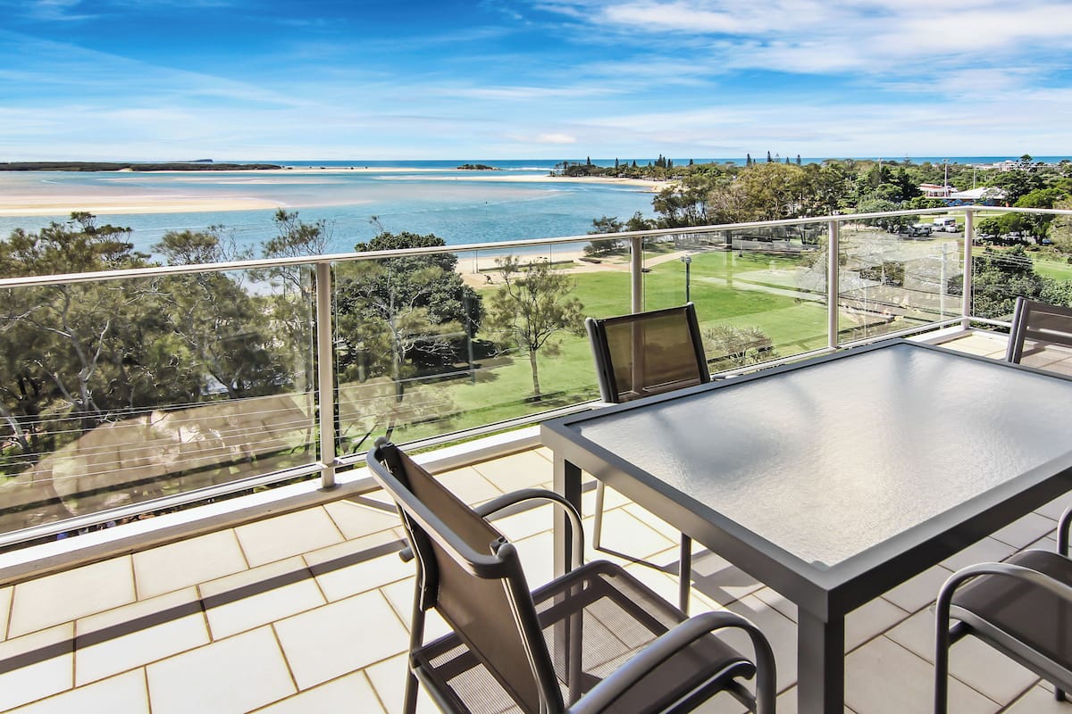 A balcony with a table and chairs, overlooking a beach and golf course.