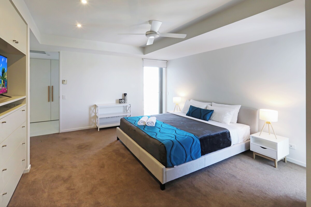 A modern bedroom with a bed, bedside tables, a ceiling fan, and a TV on a cabinet.