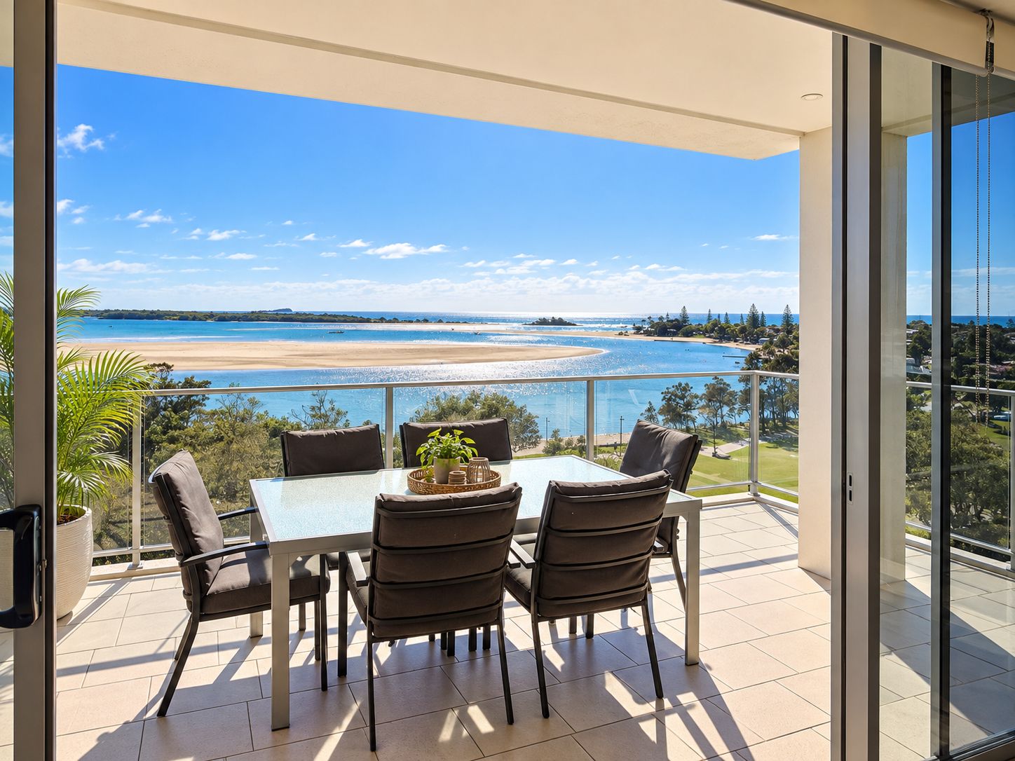 A balcony with a table and chairs, overlooking a beach and ocean.