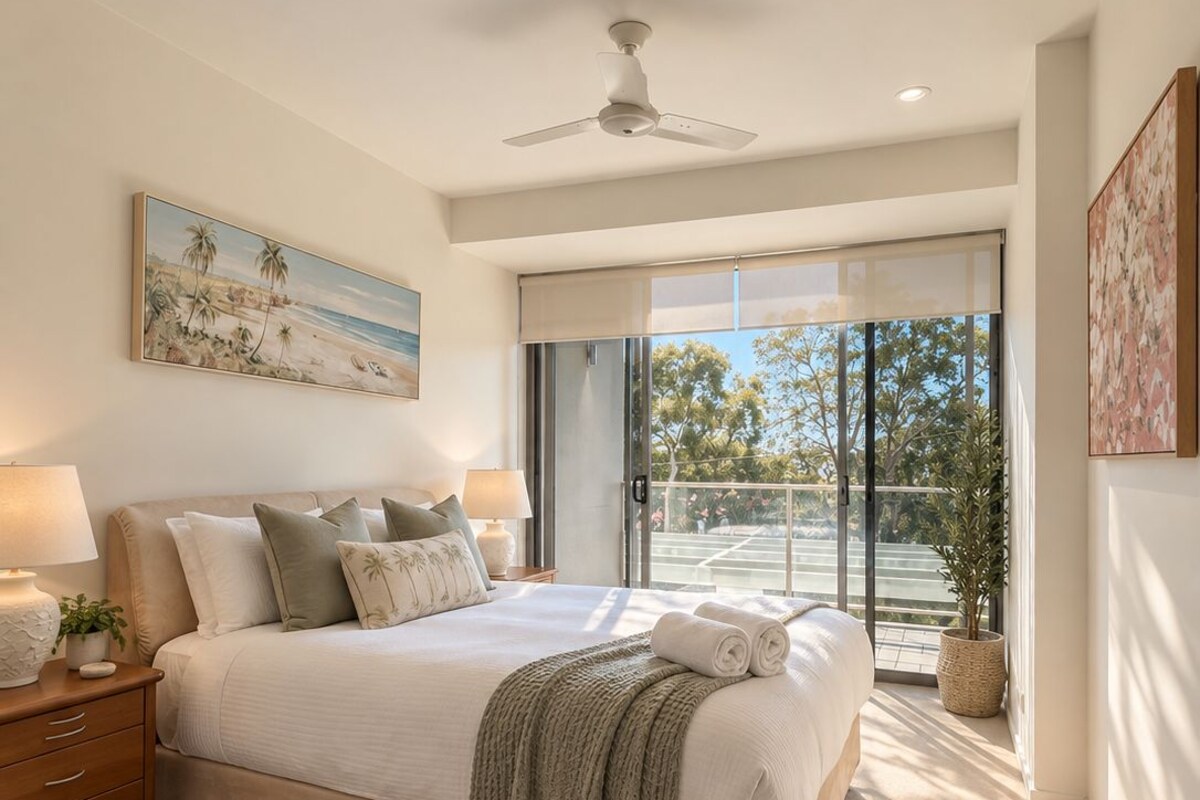 A bedroom with a bed, bedside tables, a ceiling fan, a painting, and a view through a glass door.