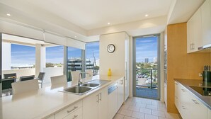 A modern kitchen with a large island, built-in dishwasher, and a view of the city through the glass door. - Space Holiday Apartments (Maroochydore)