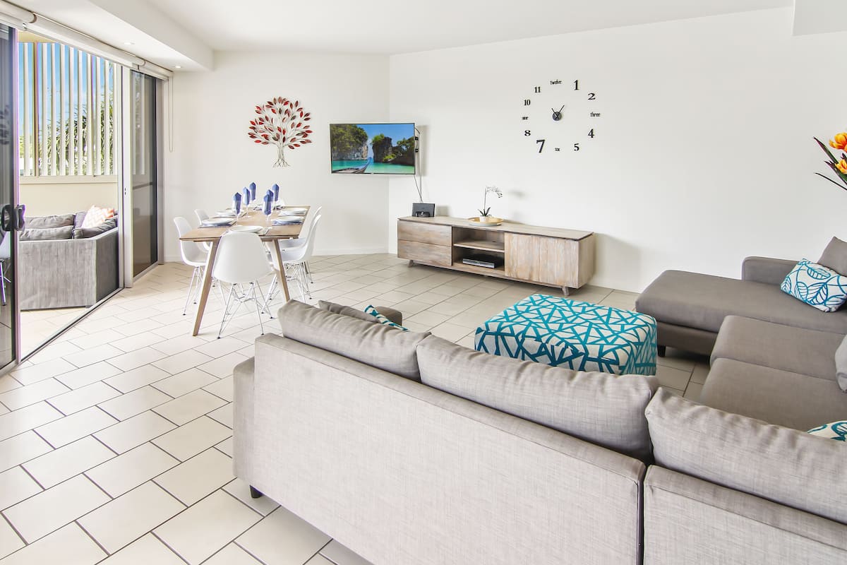 A modern living room with a sofa, dining table, chairs, and a TV.