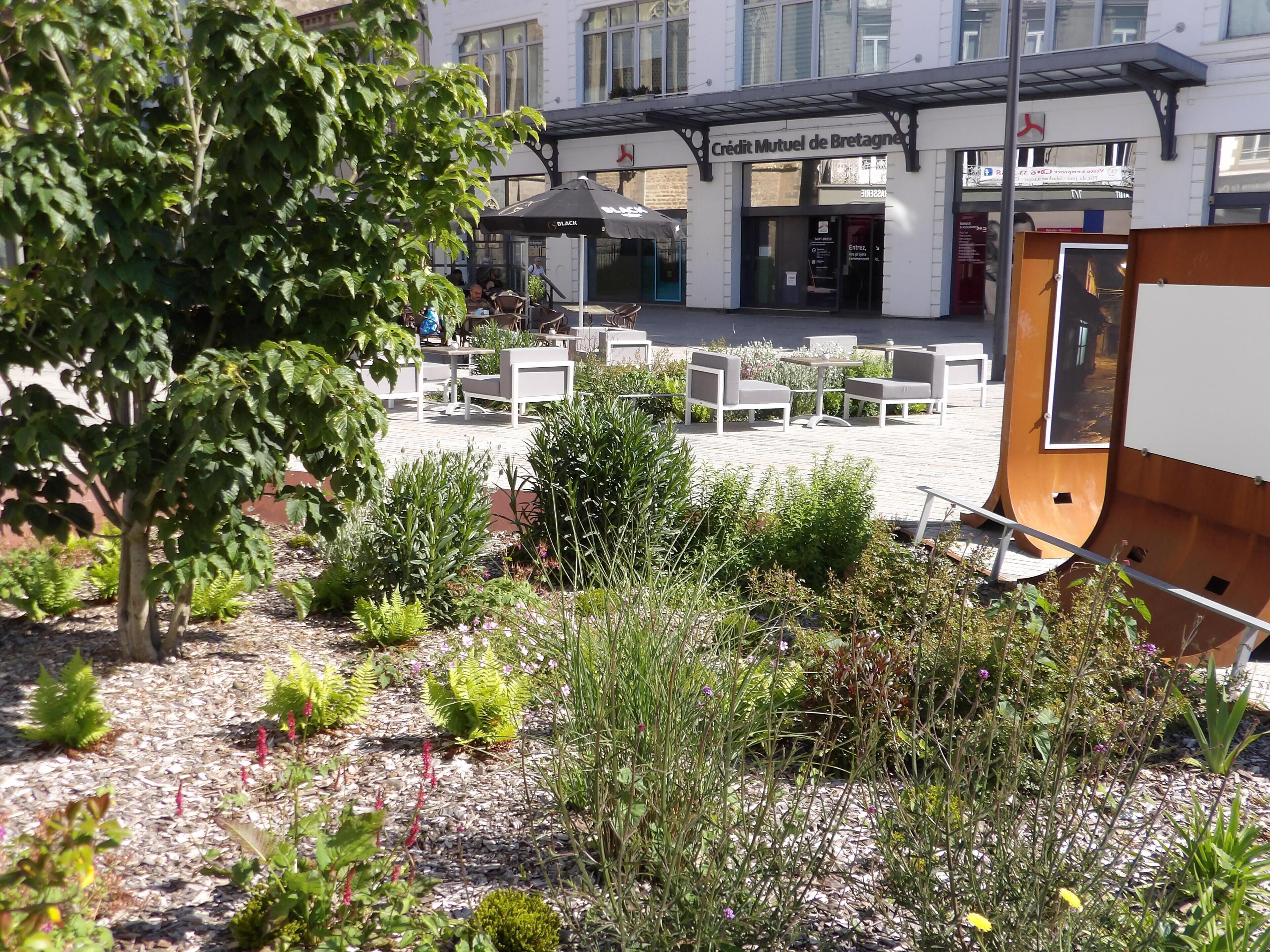 An outdoor seating area with tables and chairs, surrounded by greenery and a building with signage.