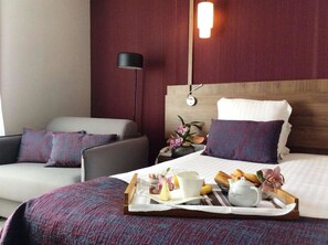 A hotel room with a bed, a bedside table with a lamp, a chair, and a tray with breakfast items. - Best Western Le Duguesclin (Saint-Brieuc)