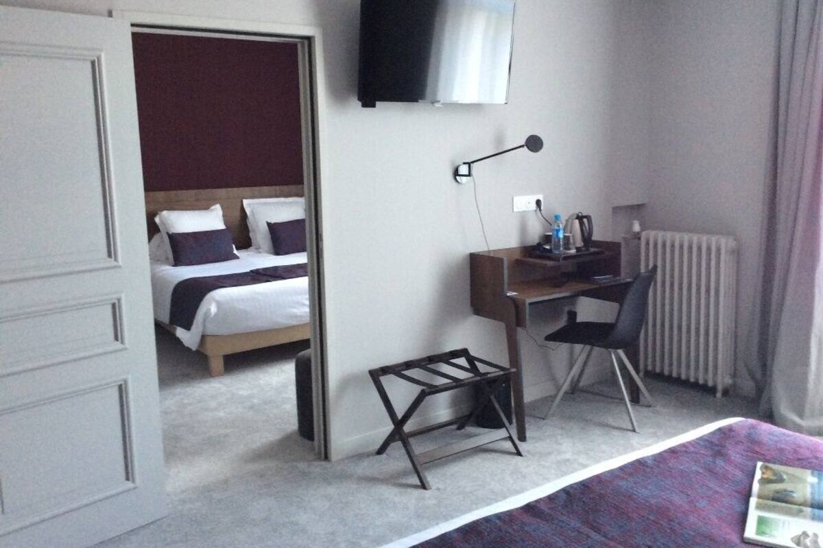 A hotel room with a bed, a desk, a chair, a TV, and a radiator.