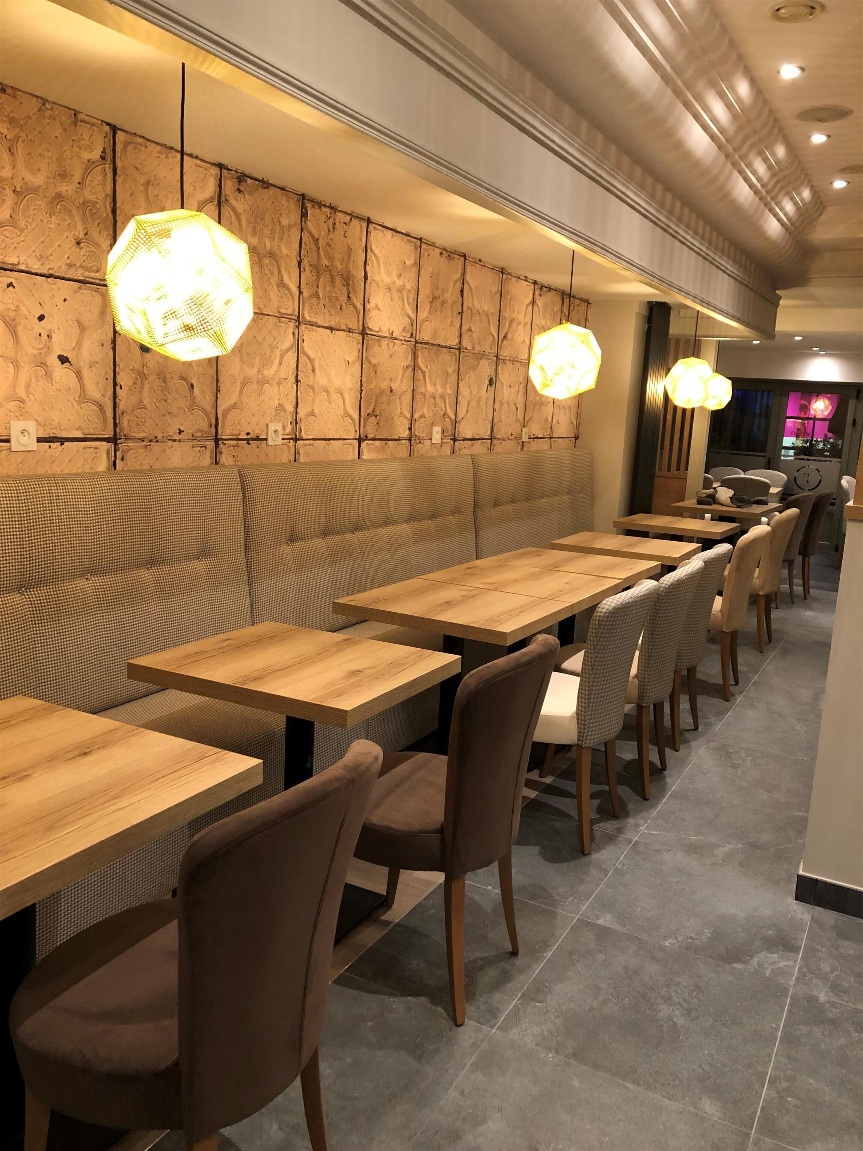 A restaurant interior with wooden tables and chairs, patterned wall, and hanging pendant lights.