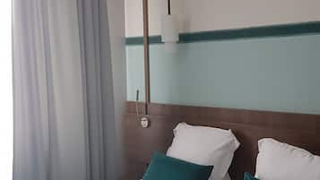 A hotel room with a bed, curtains, a wall-mounted light, and a wooden headboard.