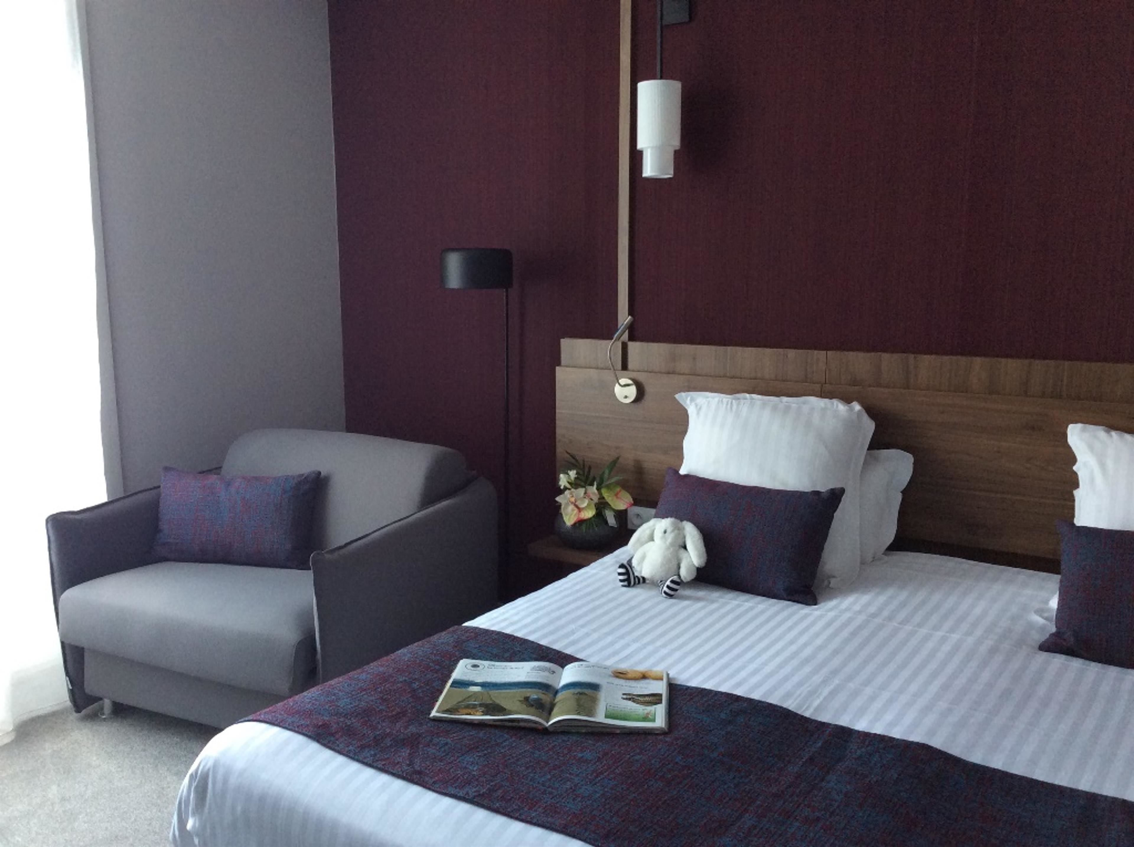 A hotel room with a bed, a chair, a nightstand, and a lamp.