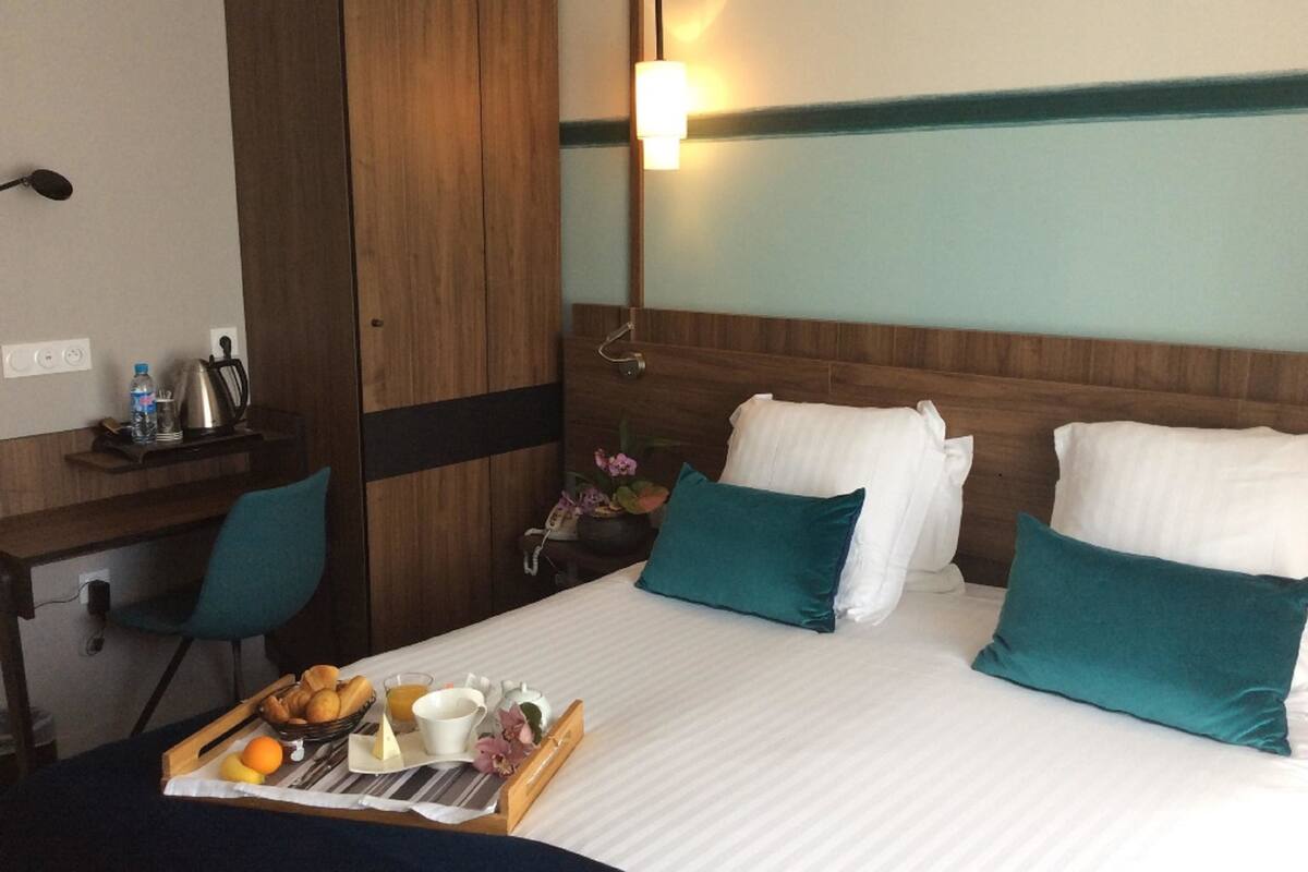 A hotel room with a bed, a desk, and a tray of breakfast items.