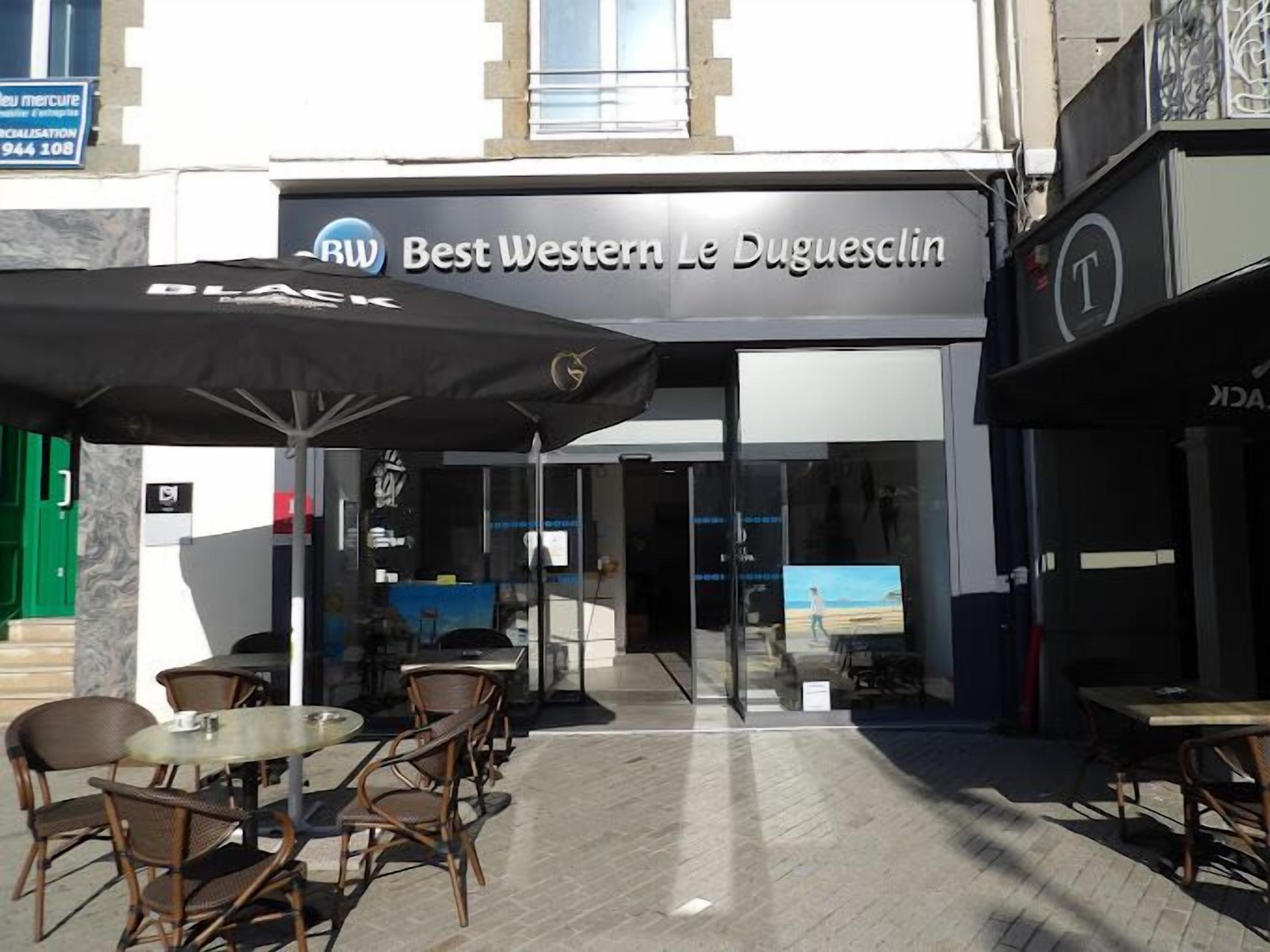 An outdoor seating area with tables and chairs, a sign for 'Best Western Le Duguesclin,' and a view of the interior through glass doors.