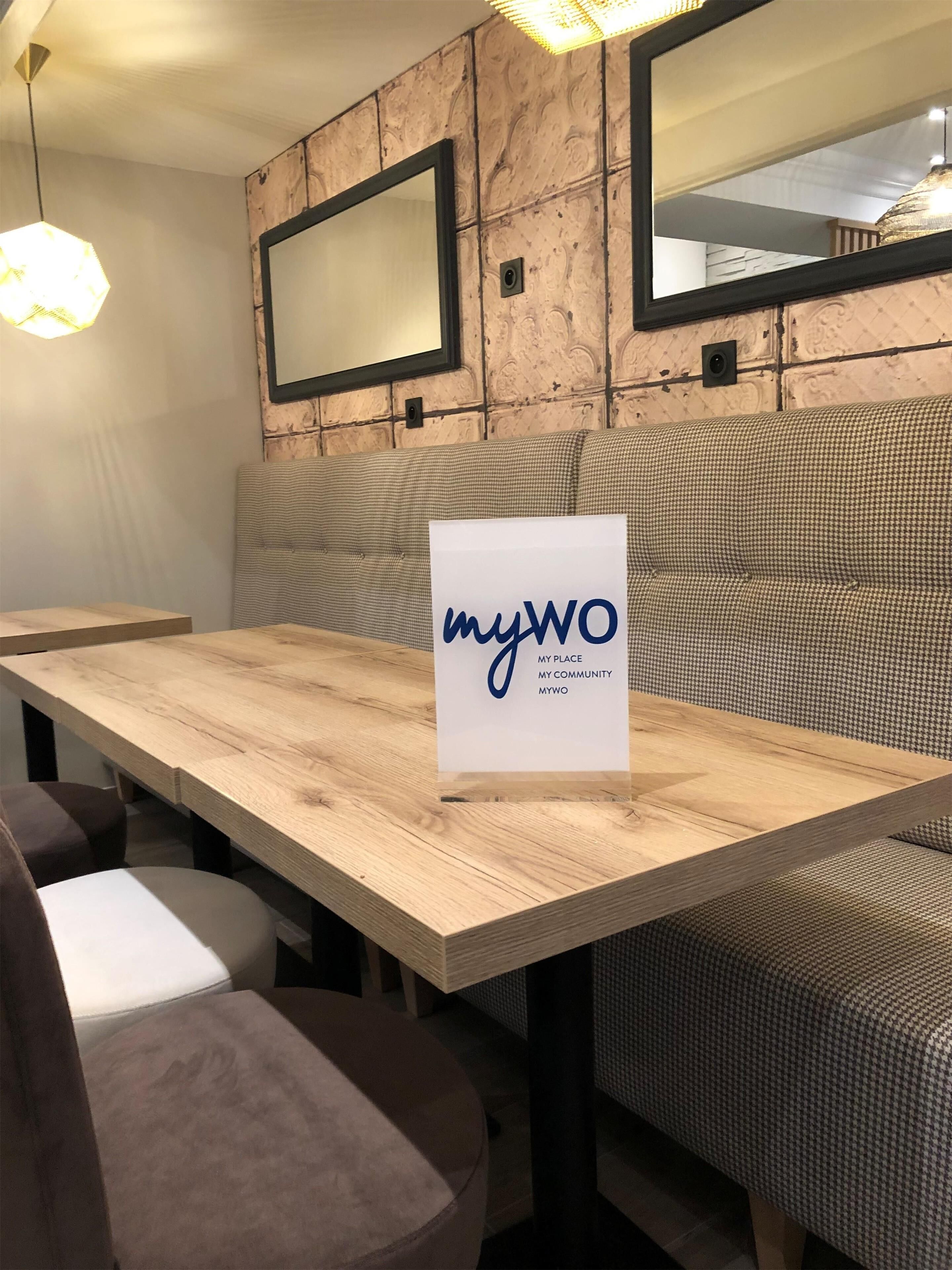 Una mesa de madera con un letrero que dice 'myWO MY PLACE MY COMMUNITY MYWO' en un interior moderno con paredes estampadas y un banco.