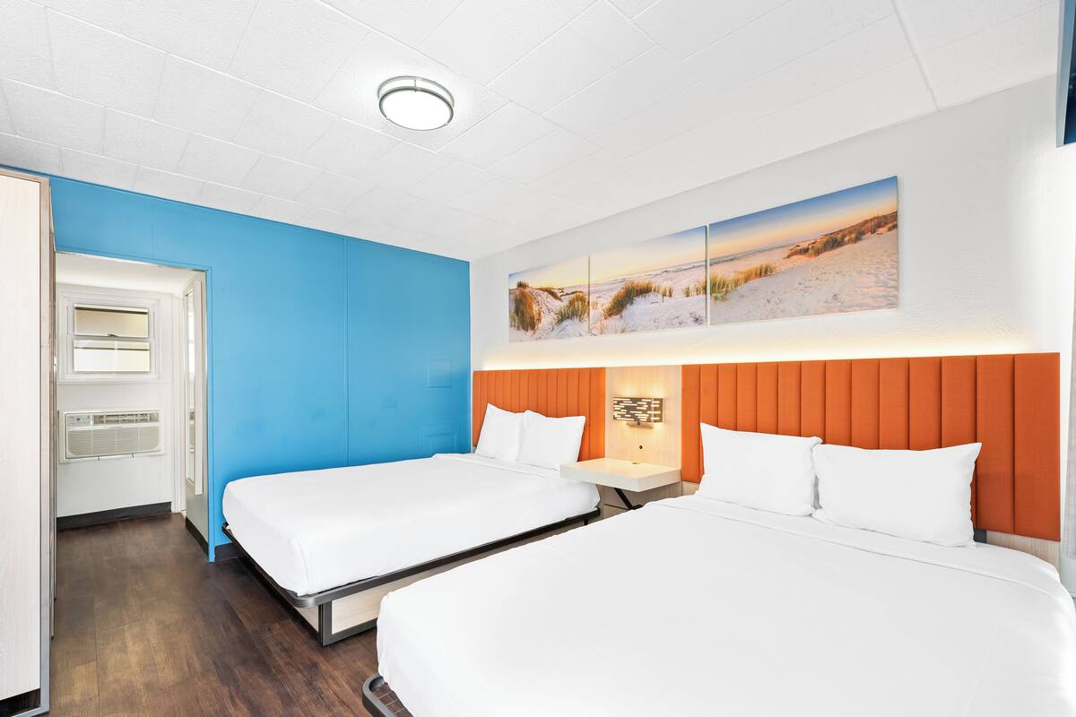 A hotel room with two beds, a blue accent wall, and a large window.