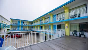 A motel with a two-story structure, a fenced courtyard, and a red car parked outside.