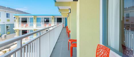 A balcony with white railings, orange chairs, and a view of adjacent buildings.