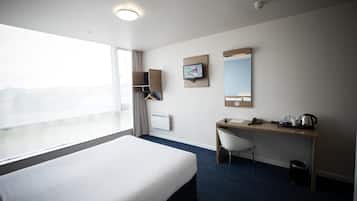 Hotellihuone, jossa on suuri sänky, työpöytä tuolilla, televisio, peili ja ikkuna, josta on näkymä.