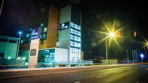 Un hotel Travelodge con fachada moderna, varios pisos y un área de estacionamiento al frente.