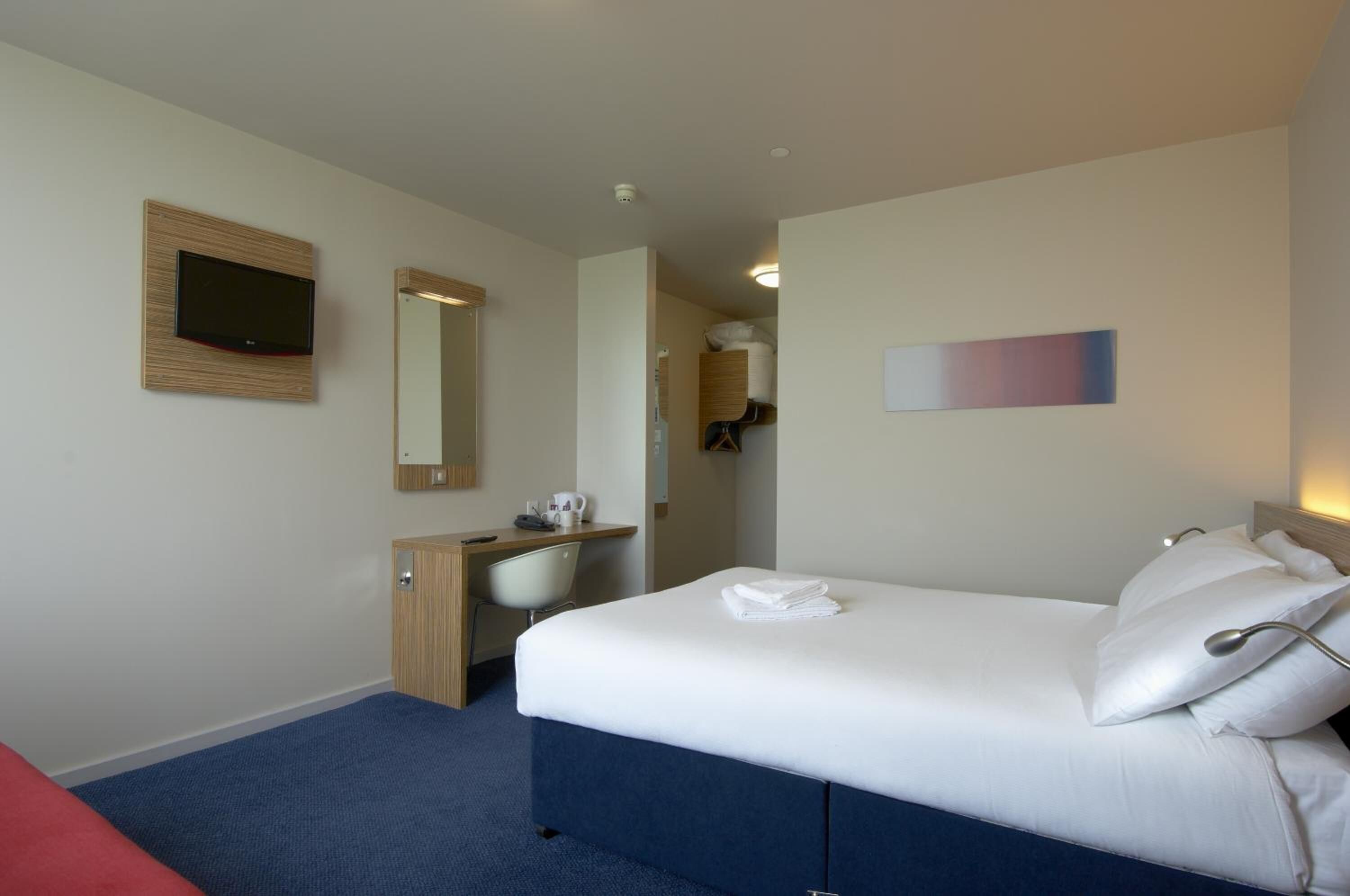A hotel room with a bed, a desk, a chair, a wardrobe, a mirror, and a television.