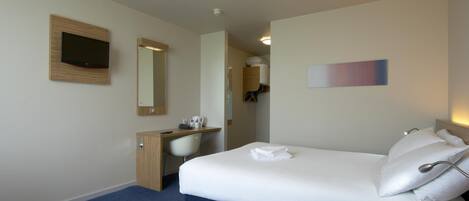 Quarto de hotel com cama, escrivaninha, cadeira, guarda-roupa, espelho e televisão.