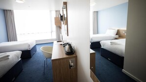 A hotel room with two beds, a desk, a chair, a minibar, and a large window.