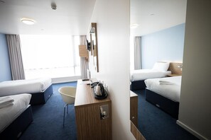 A hotel room with two beds, a desk, a chair, a minibar, and a large window.