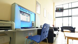 Una recepción con un letrero de Acceso a Internet, una computadora y una silla azul. En el fondo, hay dos sofás negros y una mesa de madera.