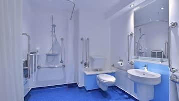 Un baño moderno con ducha, inodoro y lavamanos, equipado con barras de apoyo y una mampara de cristal.