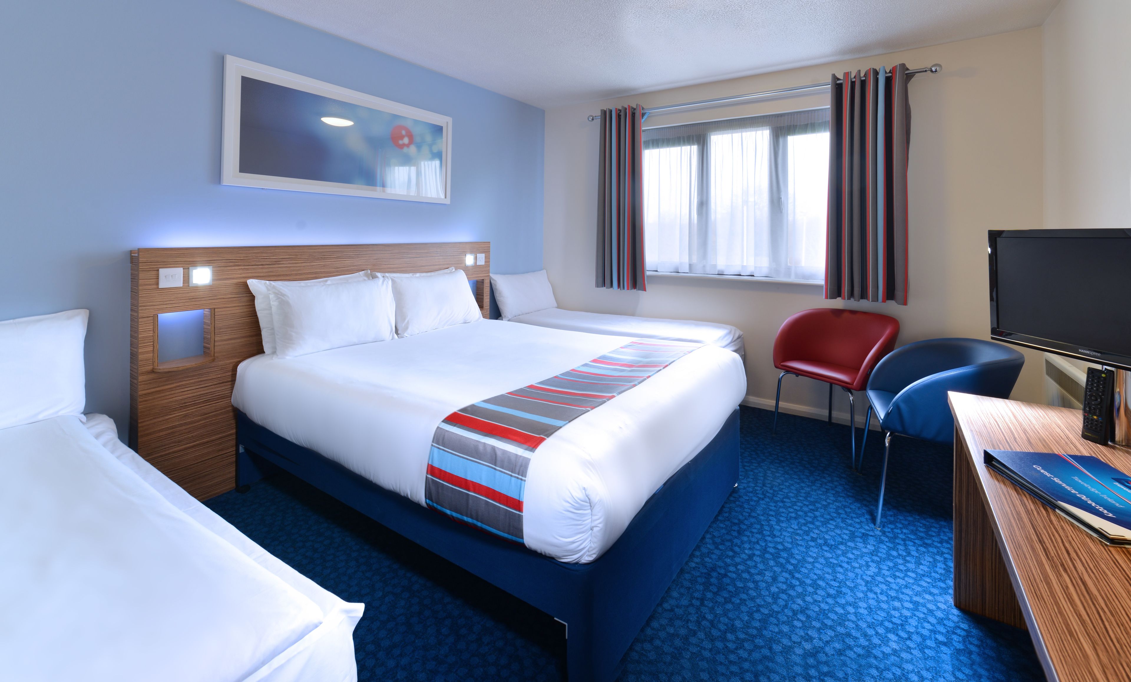 Ein Hotelzimmer mit einem großen Bett, einem Schreibtisch mit Computer, einem Sessel und einem Fernseher.