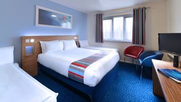 Ein Hotelzimmer mit einem großen Bett, einem Schreibtisch mit Computer, einem Sessel und einem Fernseher.