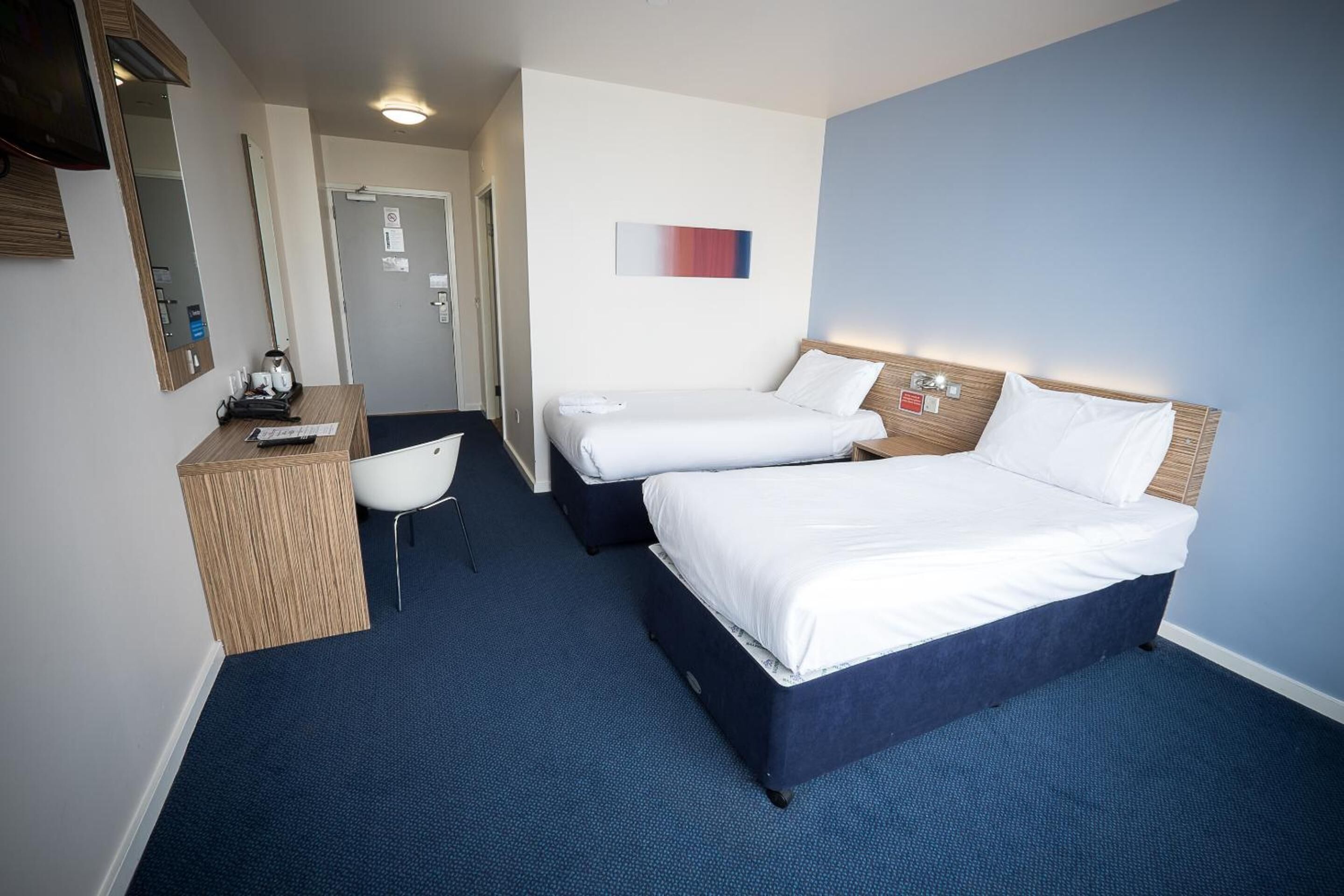 A hotel room with two beds, a desk, a chair, and a mirror.
