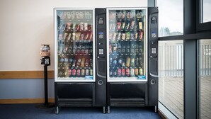 Dos máquinas expendedoras con una variedad de aperitivos y bebidas, situadas en el interior con vistas al exterior a través de una ventana.