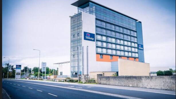 A modern building with a Travelodge sign, featuring a glass facade and a mix of orange and white colors.