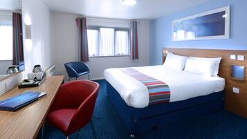 Habitación de hotel con cama, escritorio, silla, ventana con cortinas y televisor montado en la pared.