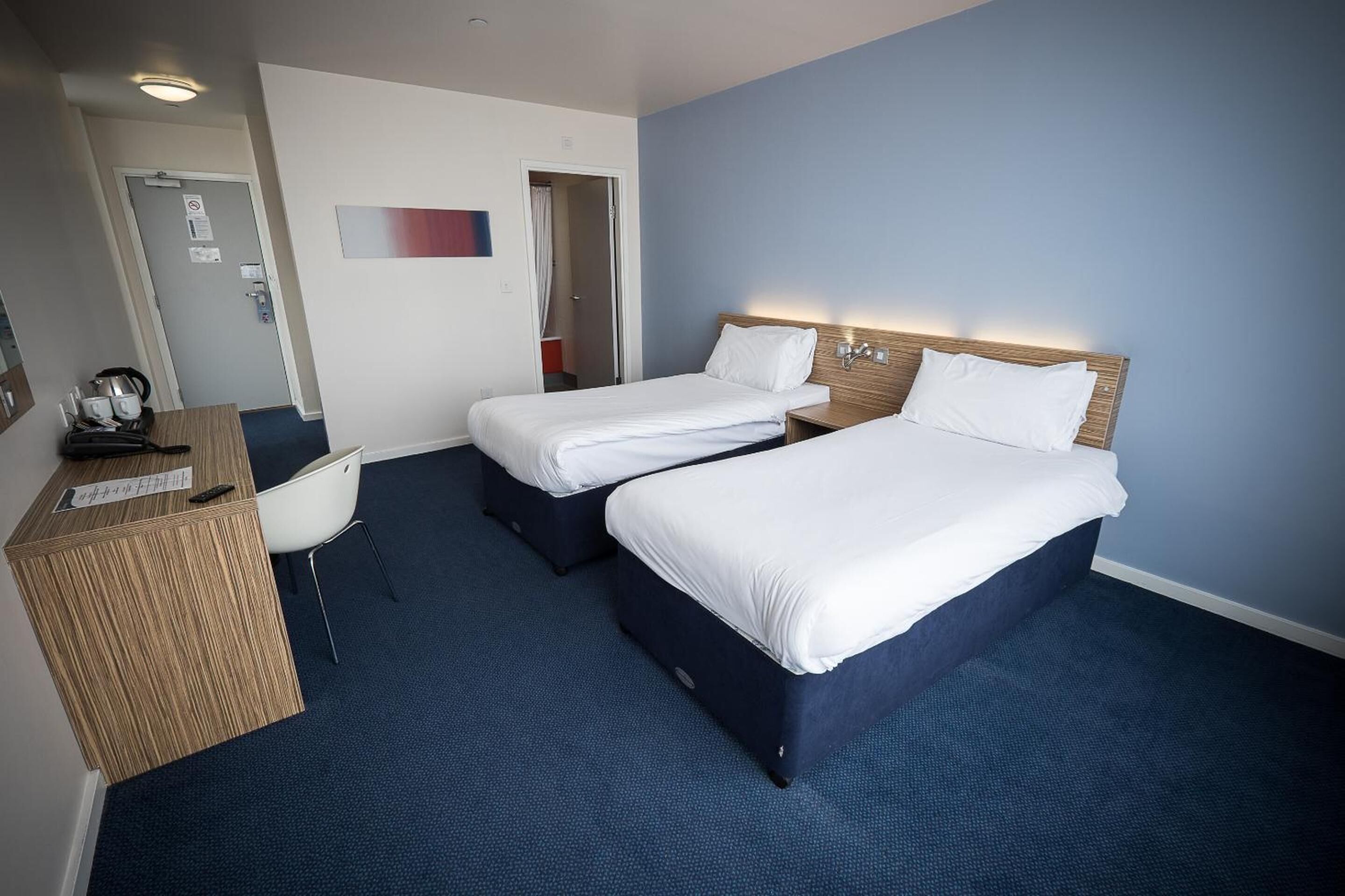A hotel room with two single beds, a desk with a computer, and a chair.