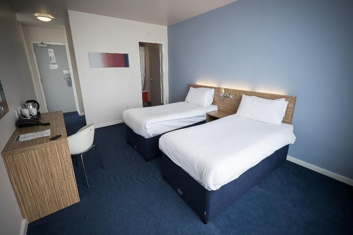A hotel room with two beds, a desk, and a chair.