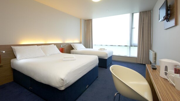 Habitación de hotel con dos camas, un escritorio con una silla, cafetera y televisor en la pared.