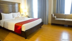 A hotel room with a large bed, a sofa, a wooden floor, and a window with curtains. - Lancaster Hotel Manila (Mandaluyong)