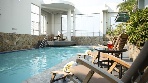 A pool area with lounge chairs and a table, stone walls, and large windows. - Lancaster Hotel Manila (Mandaluyong)