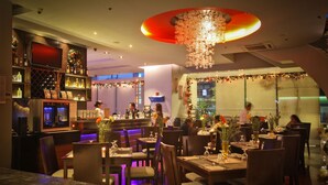 A restaurant with multiple dining tables and chairs, a bar area with a counter, and a decorative chandelier. - Lancaster Hotel Manila (Mandaluyong)