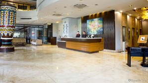 A modern hotel lobby with a reception desk, a large decorative column, and a painting on the wall. - Lancaster Hotel Manila (Mandaluyong)