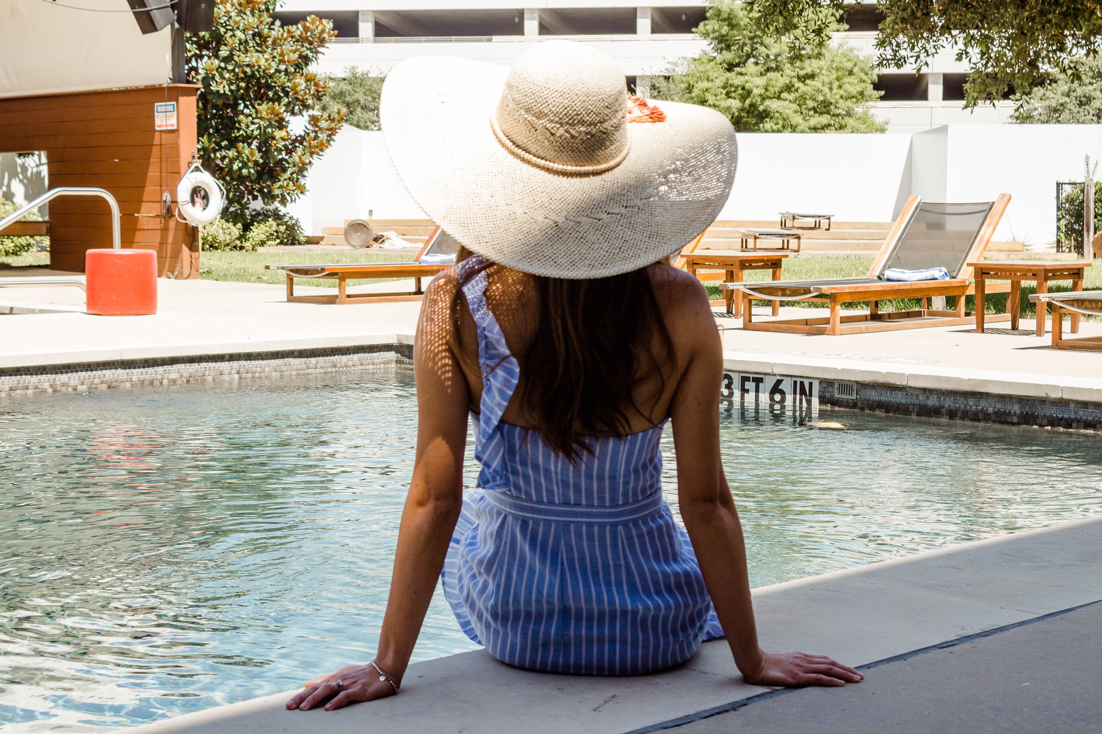 Una mujer sentada junto a una piscina con sillones reclinables y una terraza de madera.