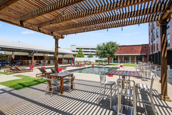 Ein Poolbereich im Freien mit Liegestühlen, Tischen und einer Pergola.